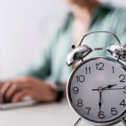 alarm clock in foreground. person on laptop in background out of focus