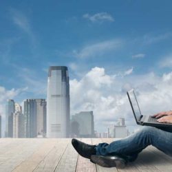 man sitting on ledge with a view, using his laptop