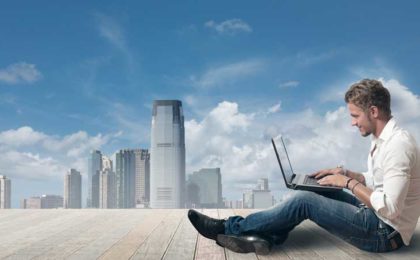 man sitting on ledge with a view, using his laptop