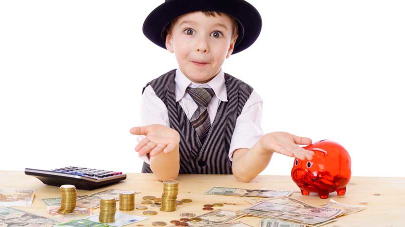 Little boy at table with piggy bank, calculator and money in the form of bills and coins