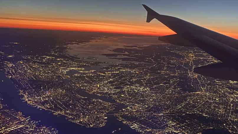 View of city from airplane with horizon turning orange from sunrise