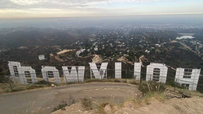 Large sign from behind that says Hollywood backwards and a hilltop view beyond