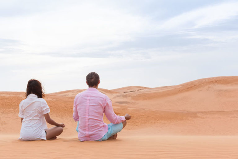 Two people sitting on sand and meditating