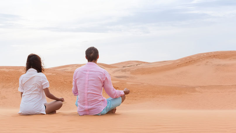 Two people sitting on sand and meditating