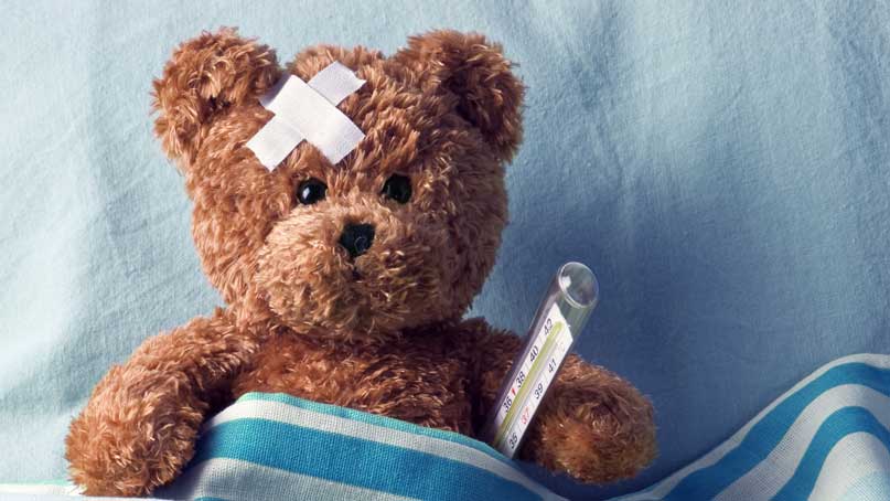Teddy bear in a blanket with thermometer and bruise on head