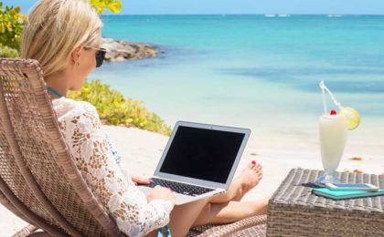 woman sitting on a lounge chair at the beach with a laptop