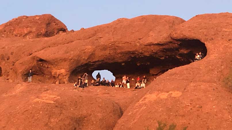 rock with a hole and many people watching the sunset
