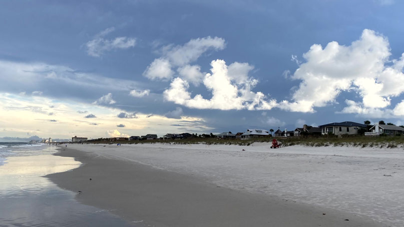 View up a long beach, with dark and light clouds above