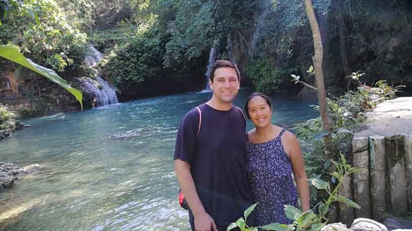 two people standing in front of a lake and small waterfall