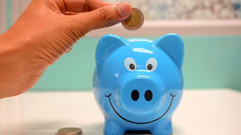 hand putting a coin into a piggy bank