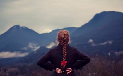 woman with hands behind back looking at mountains in the distance
